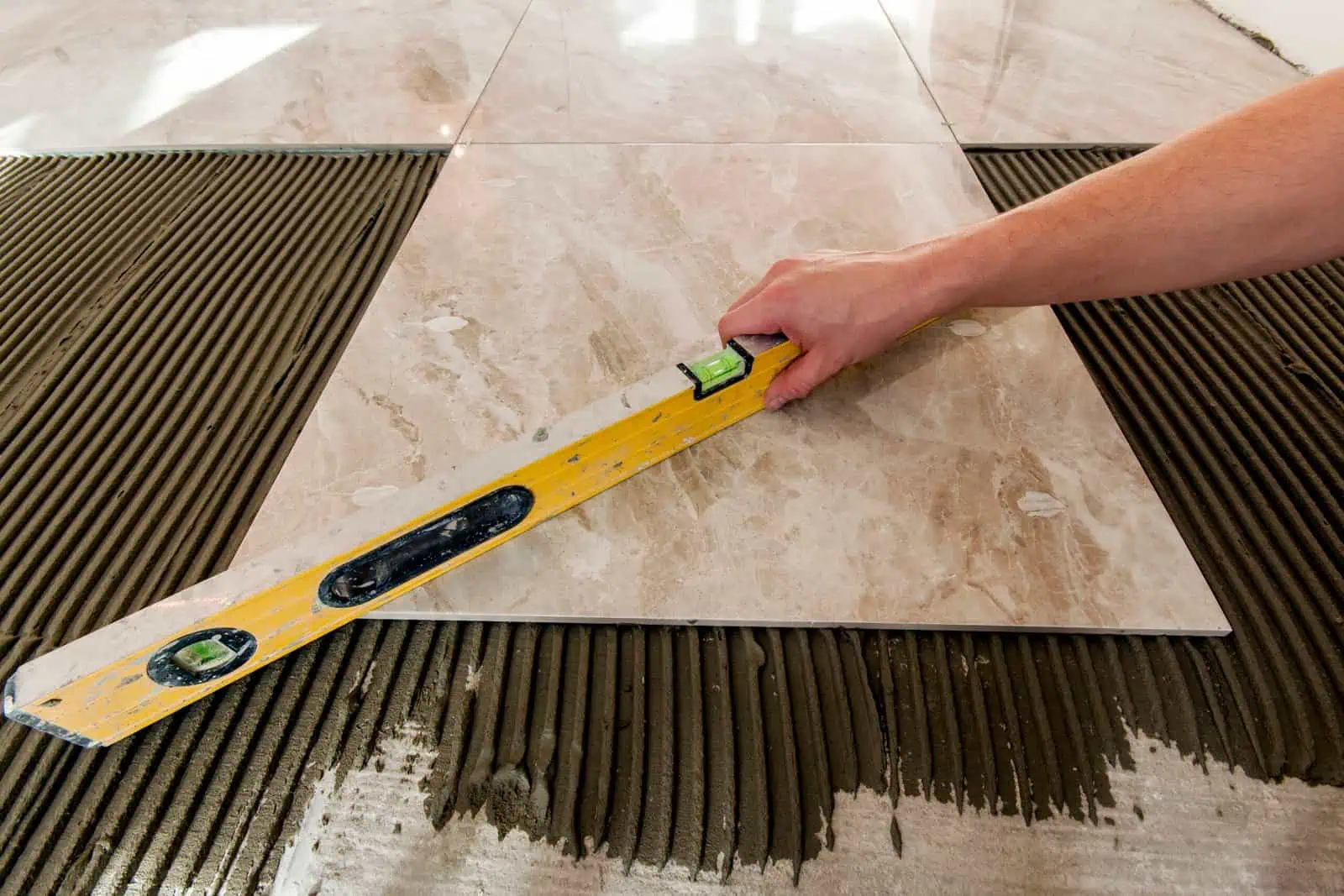 Alt: Close-up of marble tile being installed, showing precise measuring and cutting for flooring.